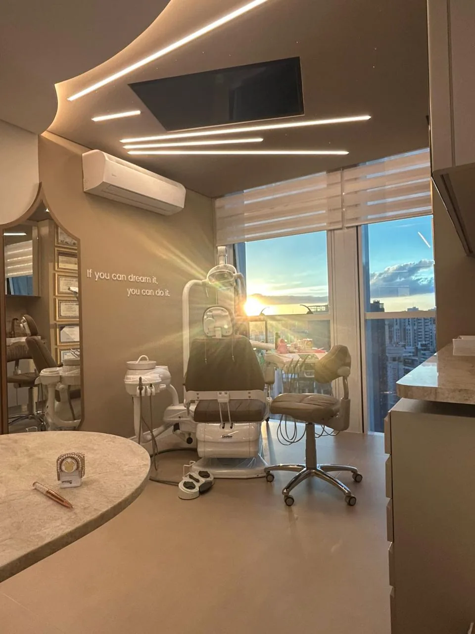 Consultório odontológico com cadeira, equipamentos modernos, iluminação suave e vista panorâmica ao pôr do sol