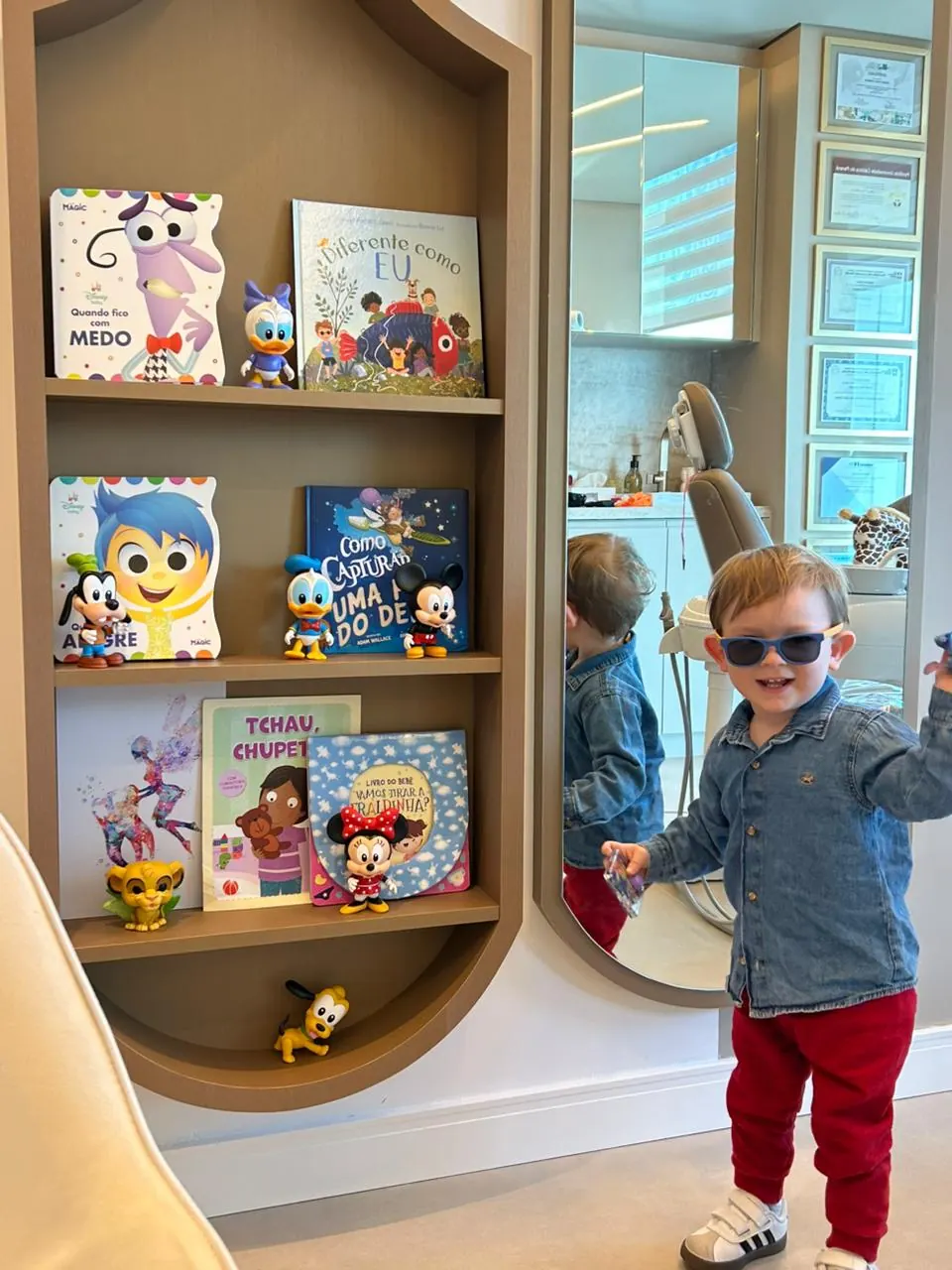 Criança sorrindo ao lado da estante de livros infantis do consultório